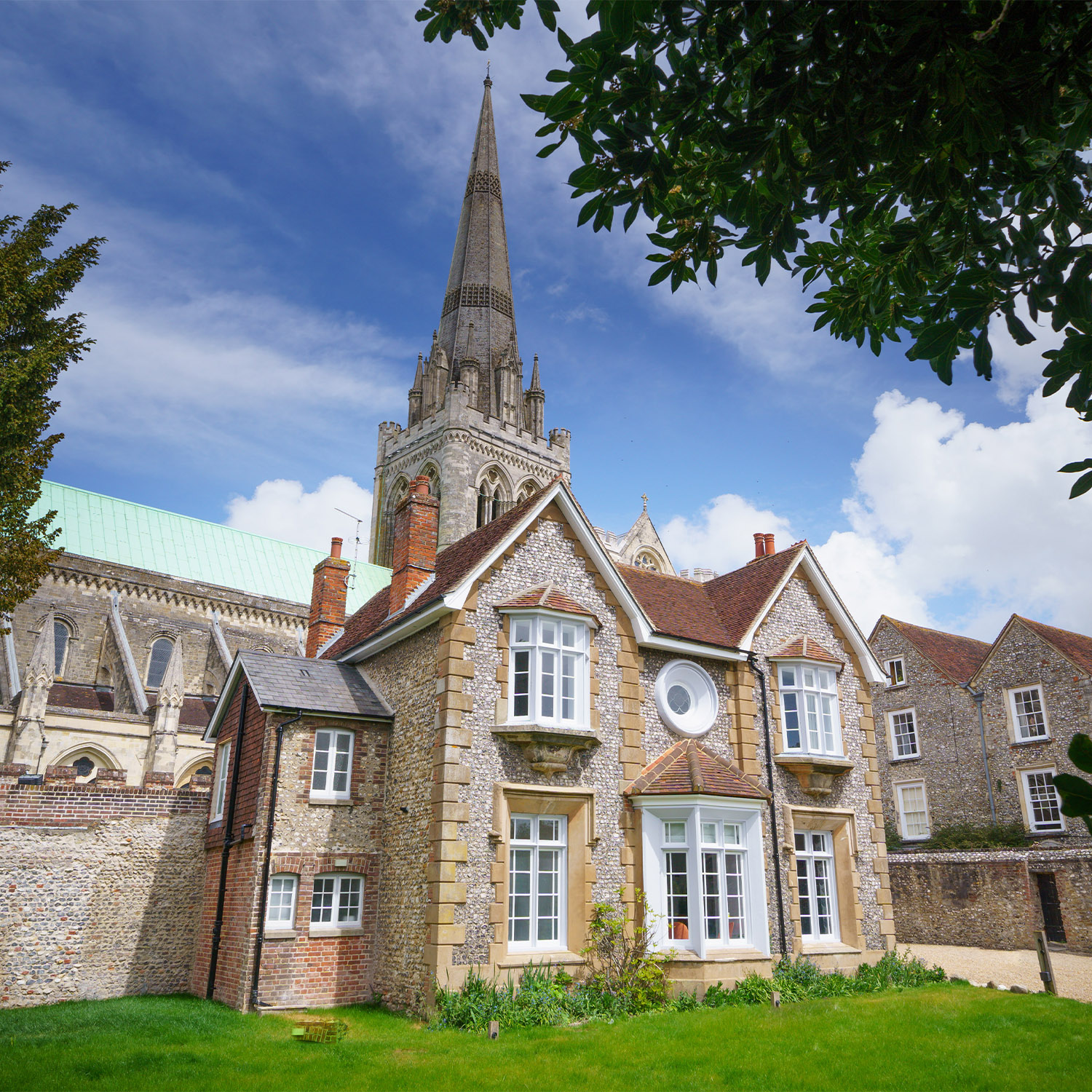 A stone building stands against a bright blue sky, and the Cathedral spire in the background