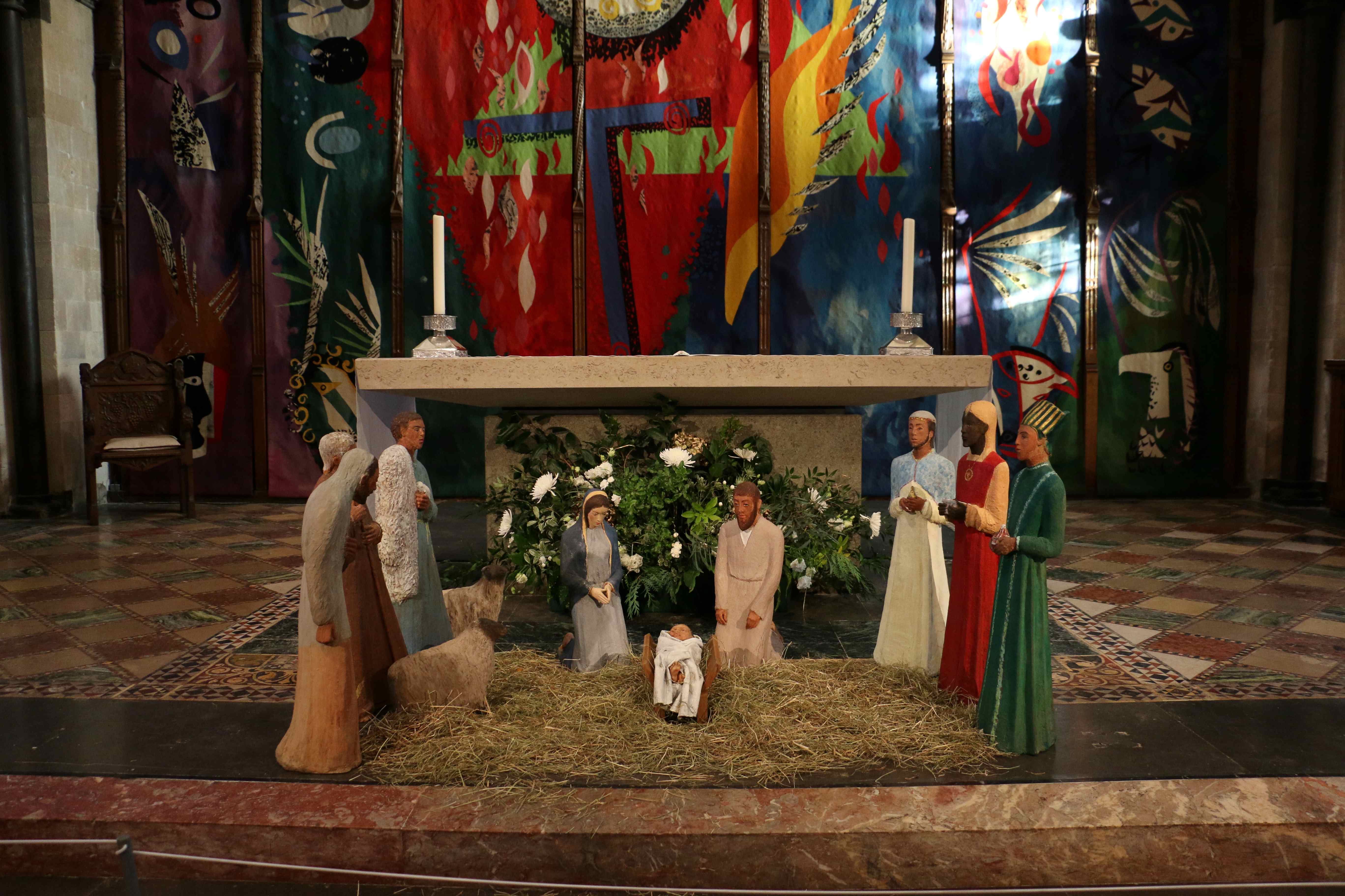 Nativity figures in front of the High Altar in the foreground, bright coloured tapestry in the background