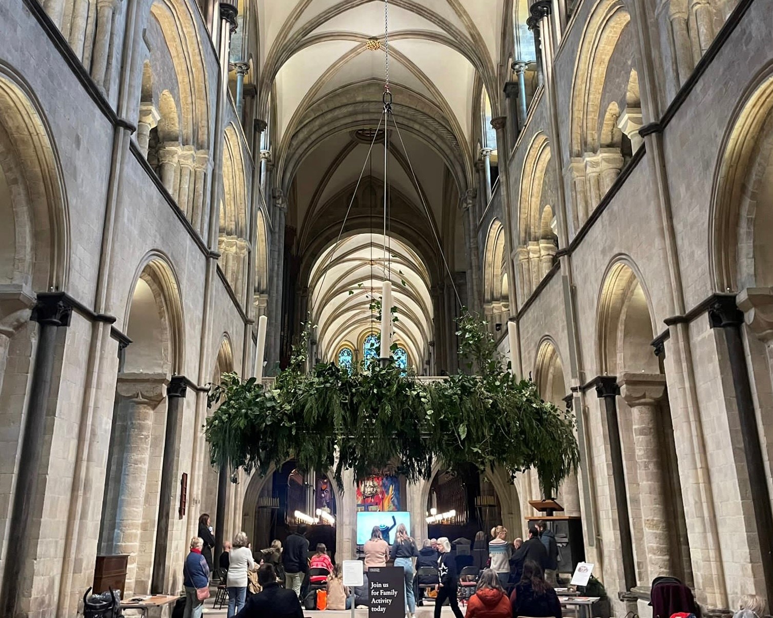 People sit at the front of the Cathedral Nave, in front of the Advent wreath and listen to Interim Dean reading a story.