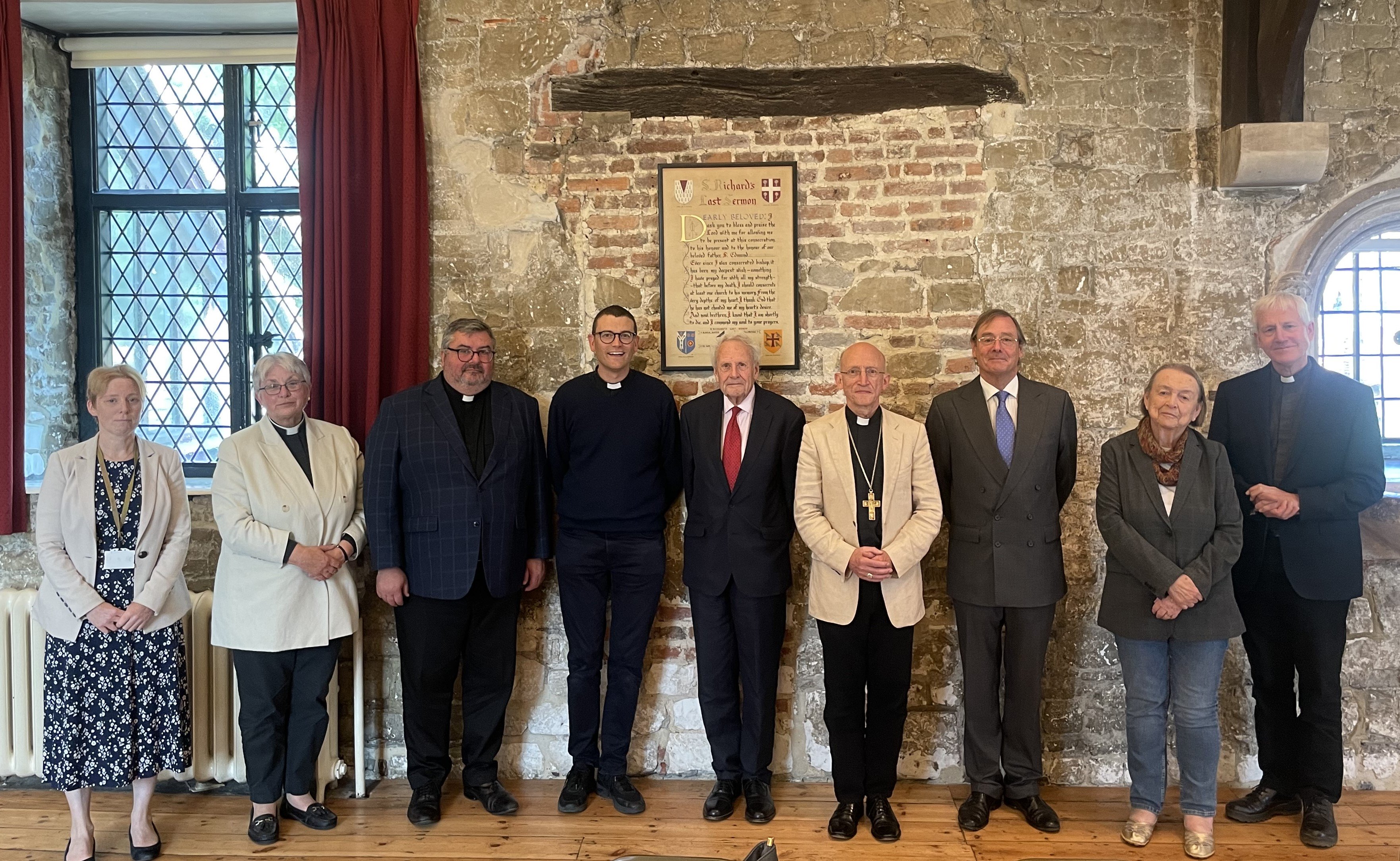 9 people, including the Rt Revd Dr Martin Warner, Bishop of Chichester, stand in front of a stone wall