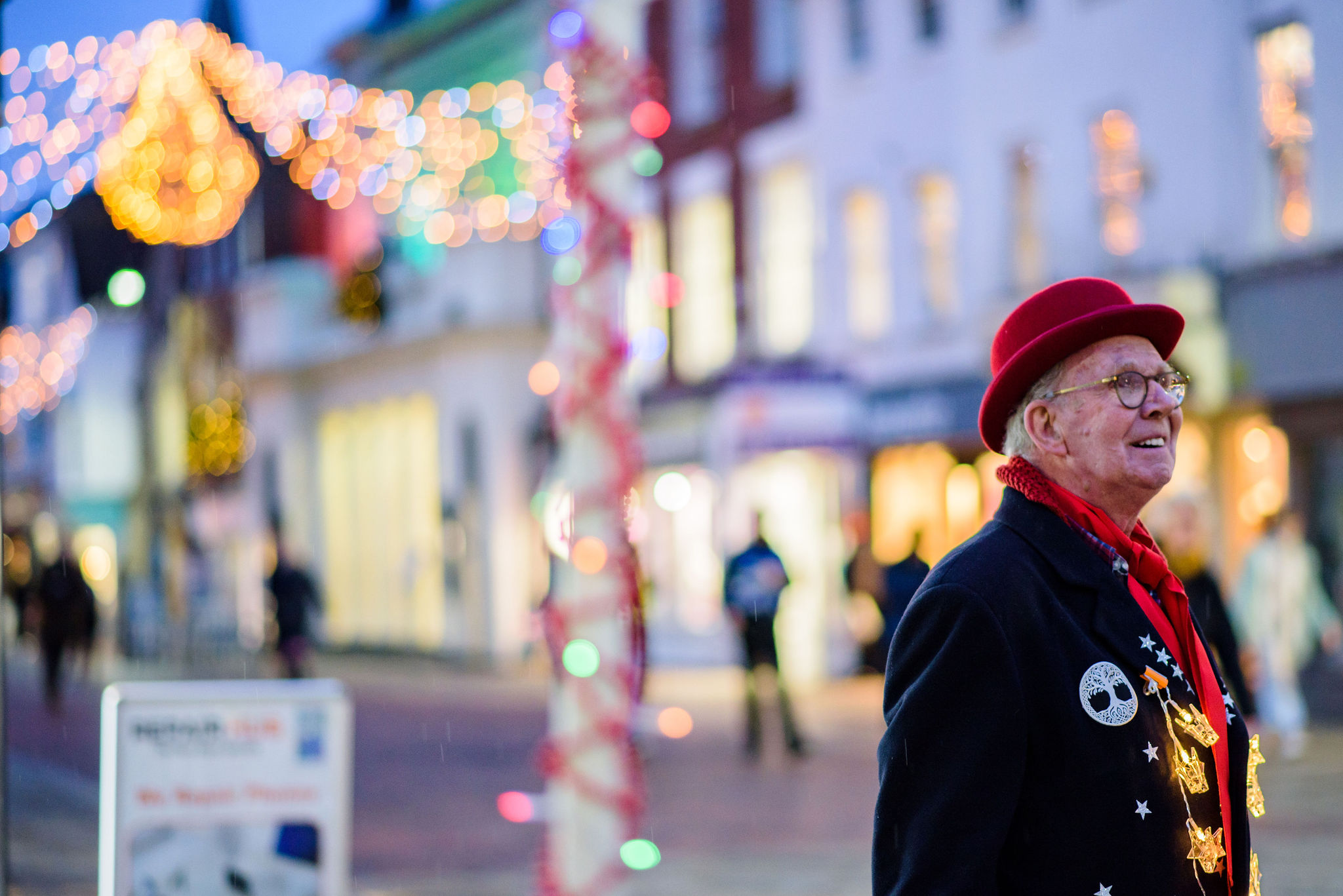 Chris North, wears a red hat, scarf and black glasses - smiling and looking off camera